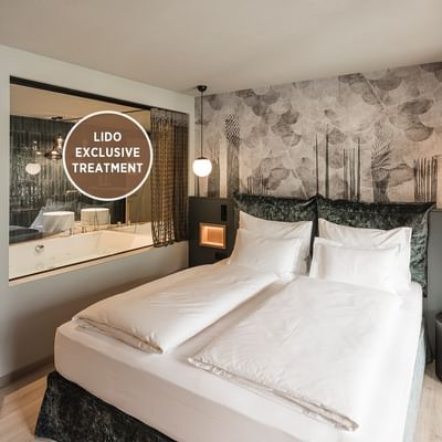 Modern hotel room with twin beds, wall-mounted lamps, and a bathroom with a large mirror.