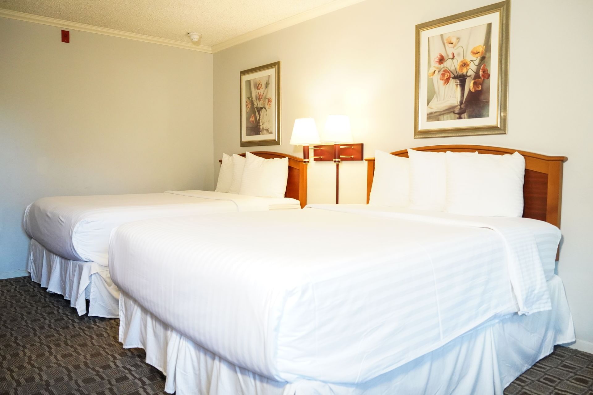 A hotel room with two beds, wooden headboards, and framed artwork on the walls.