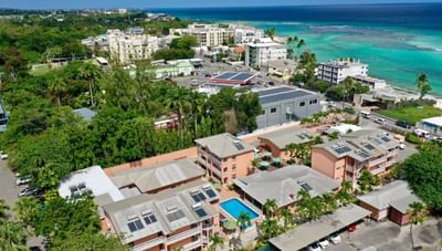 Aerial view of pink resort buildings with a swimming pool and tropical trees near the ocean at Worthing Court Apartment