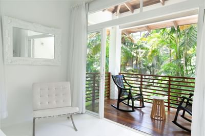 Deluxe Room - King Bed with rocking chair and balcony view of lush greenery at Le Cameleon Boutique Hotel