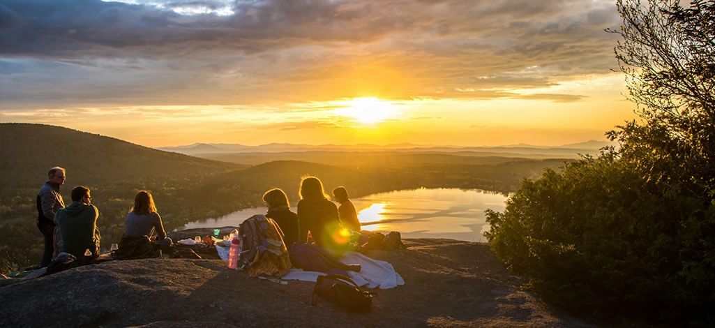 Friends enjoying a picnic on a cliff at sunset overlooking a lake