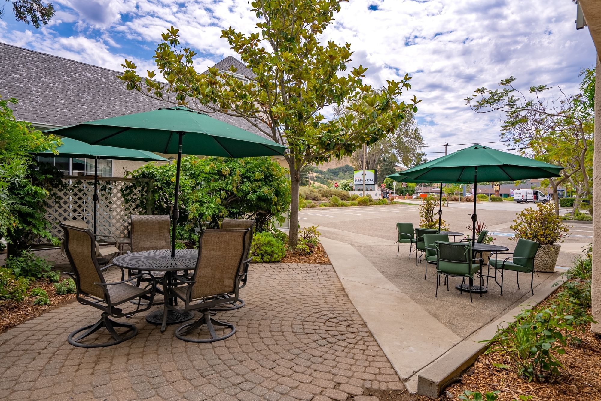 A small outdoor seating area with green umbrellas and tables surrounded by trees and brick pavers.
