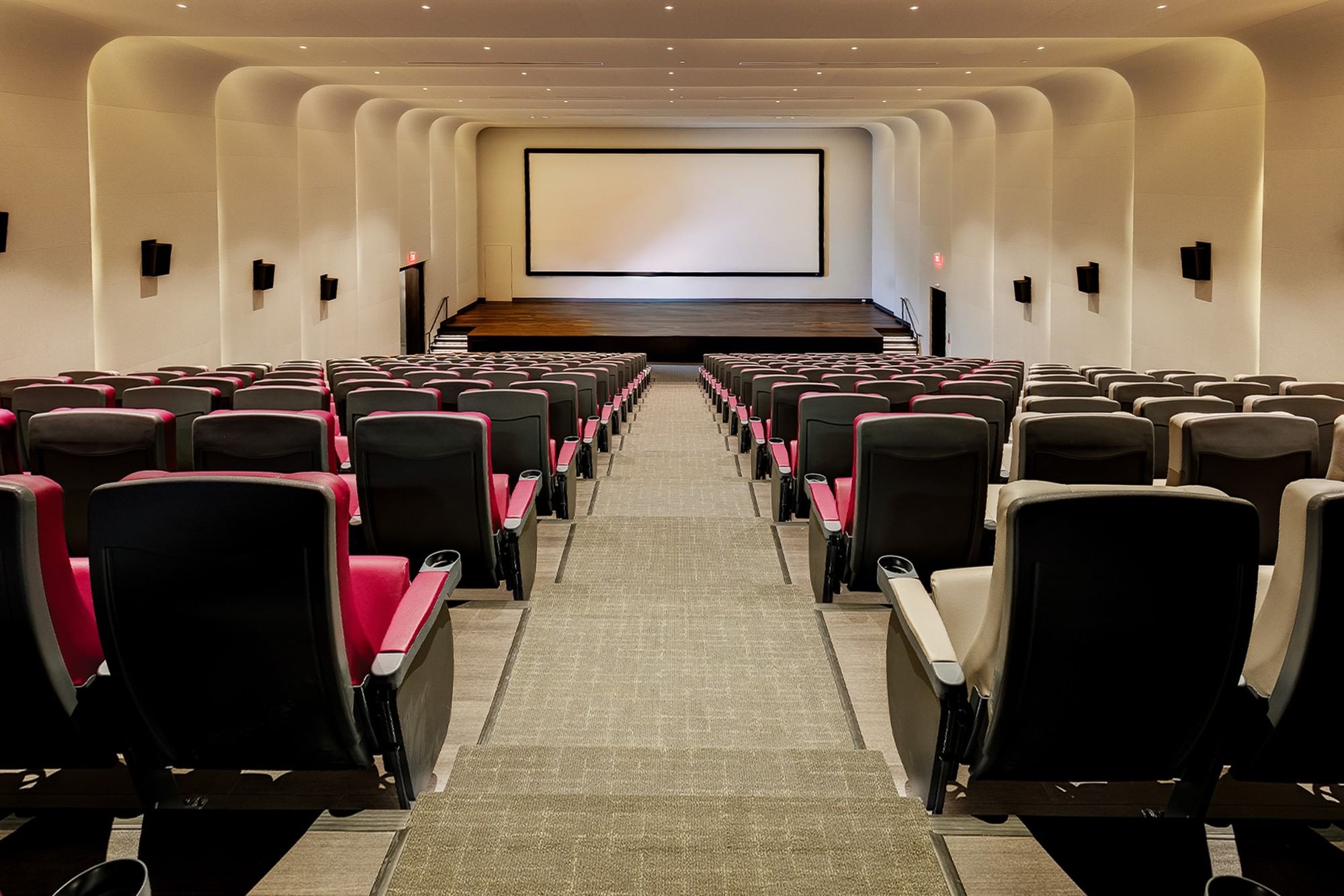 Cinema  with pink and gray tiered seats faces a stage with a white sofa and screen at Hotel X Toronto