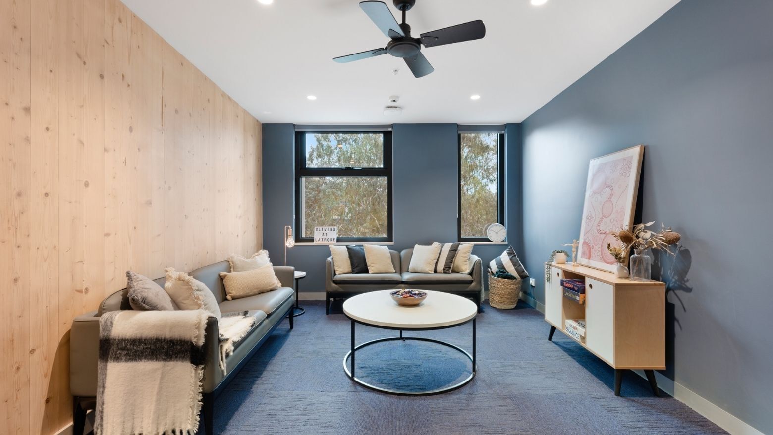 Modern living room with couches, coffee table, and ceiling fan at La Trobe University - North and South Apartments.