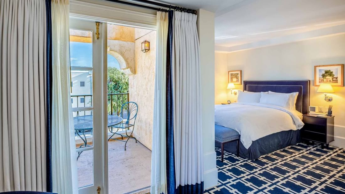 Deluxe Queen Room with a private balcony, large bed, and bold blue patterned carpet at El Prado Hotel