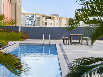 Outdoor pool with surrounding greenery and wooden furniture at Student Living Auckland Anzac.
