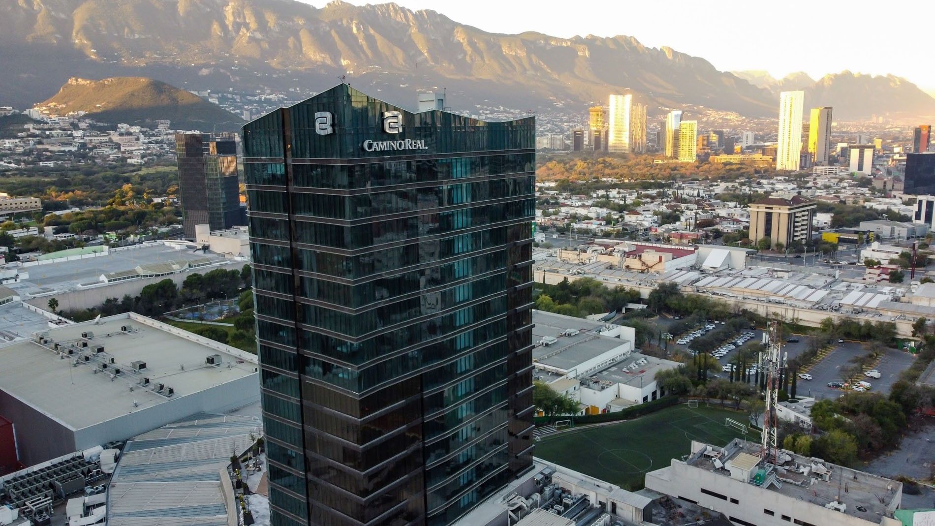 Aerial view of the Camino Real Fashion Drive Monterrey hotel, a glass skyscraper with mountains in the background