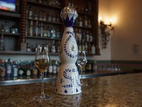 A decorative bottle and glasses of amber tequila on Bar La Suerte at Hacienda del Mar Los Cabos