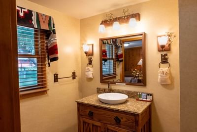 Well-lit bathroom vanity with a unique bowl sink, wooden cabinet, and warm lighting in Aspen Cabins at The Ranch at UCross