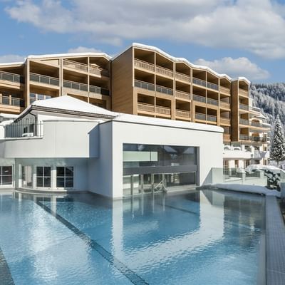 Modernes Gebäude mit Pool, umgeben von schneebedeckten Bergen und Wolkenhimmel.