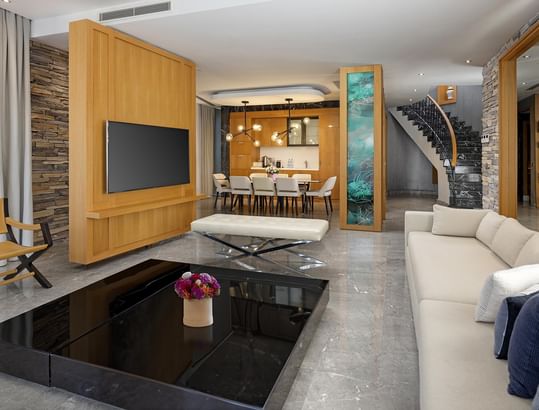 Superior Villa's modern living room with couch, coffee table, TV, dining area, and staircase, showcasing contemporary design elements at Titanic Luxury Collection Bodrum