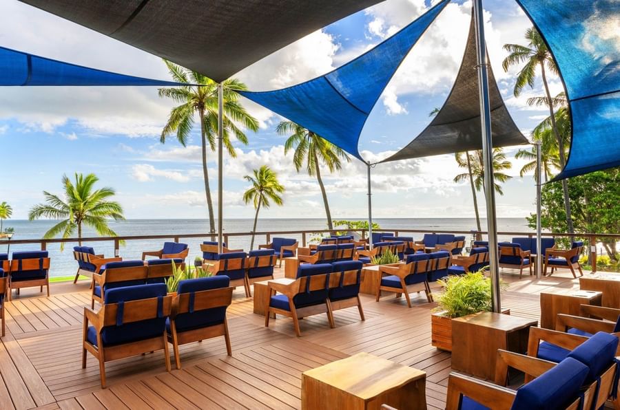 Blue lounge chairs on a wooden deck under a canopy by the ocean in Nukunuku Restaurant & Bar at The Naviti Resort - Fiji