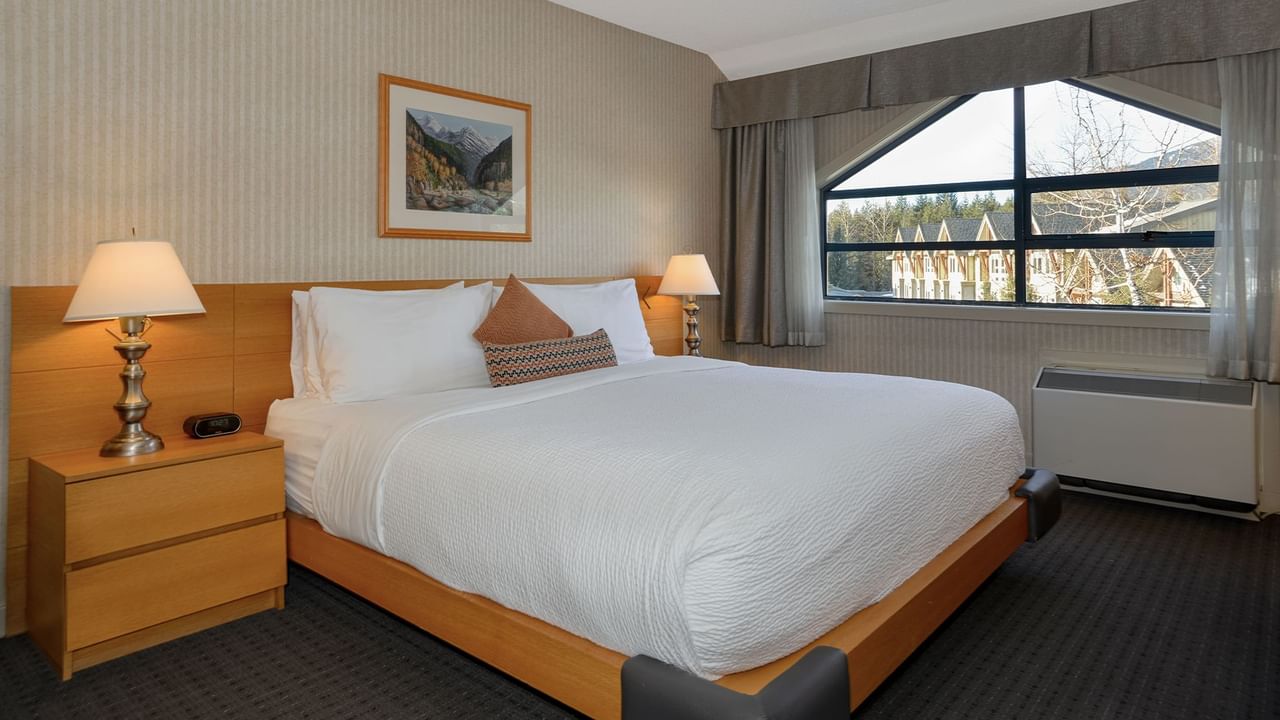 Spacious hotel suite with a king bed, elegant decor, and a large window.