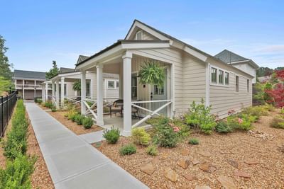 Modern cottage with porches, landscaped gardens, and a paved walkway under a clear blue sky by Cottages at Laurel Brooke