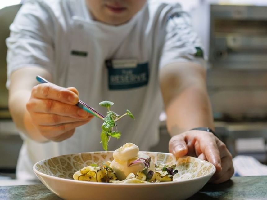 Chef delicately garnishing a dish of gnocchi and greens with tweezers at Amora Hotel Riverwalk Melbourne