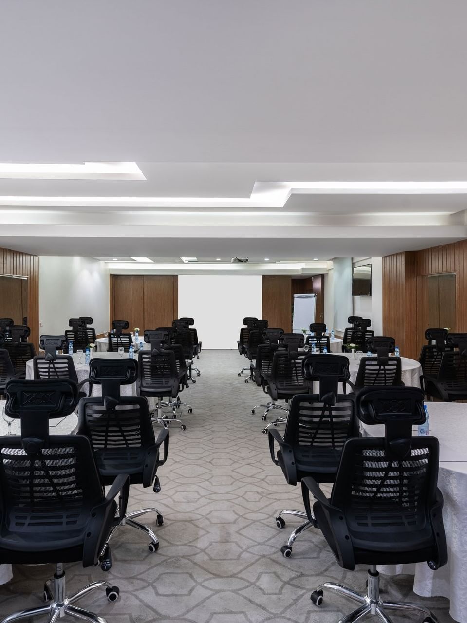 Round tables with rolling chairs facing a projector screen in Meeting Room B at Warwick Hotel Jeddah