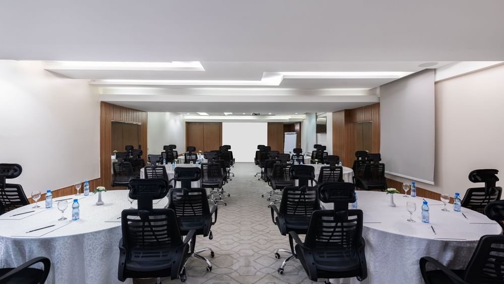 Cabaret set-up with black mesh chairs facing the projector screen in Meeting Room B at Warwick Hotel Jeddah