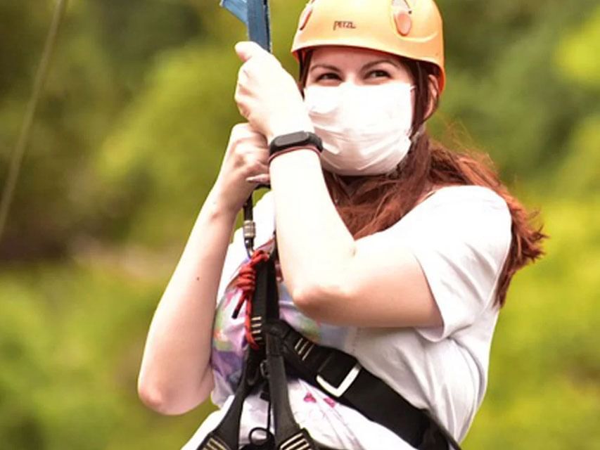 Lady in a helmet holding onto a zip line pulley with a safety harness on near The Terraces Resort & Spa