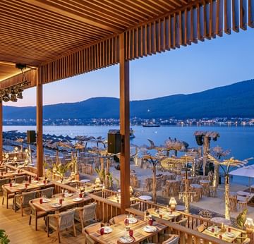 Wooden outdoor dining area with sea and mountain views at sunset at Titanic Luxury Collection Bodrum.
