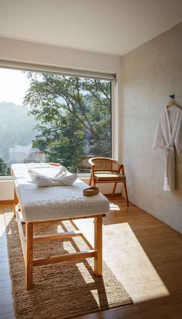 Spa room with a massage bed, and a large window overlooking lush greenery at The Terraces Resort & Spa