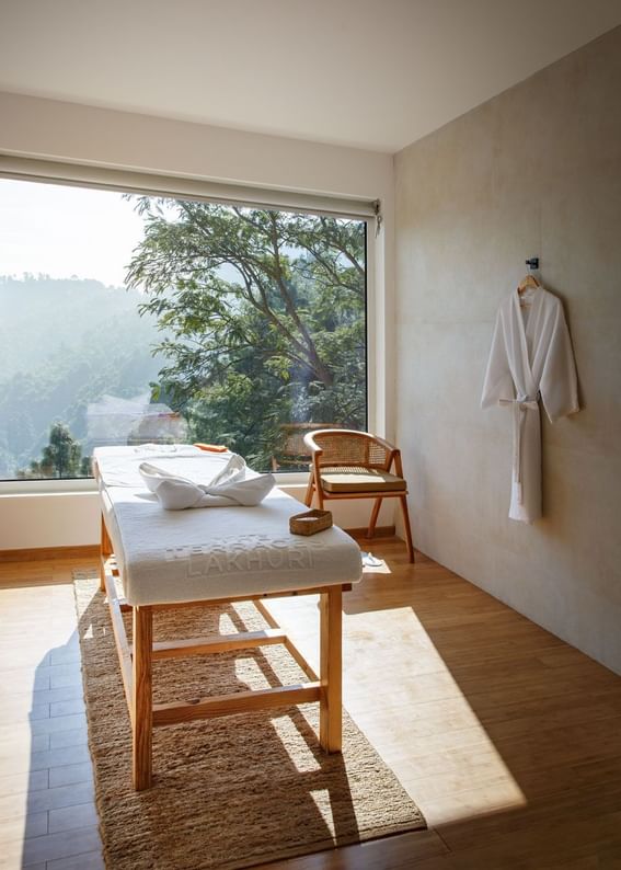 Spa room with a massage bed, and a large window overlooking lush greenery at The Terraces Resort & Spa