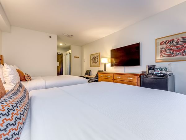 Two beds with pillows, a TV, and a framed Indigenous artwork on the wall in a hotel room.