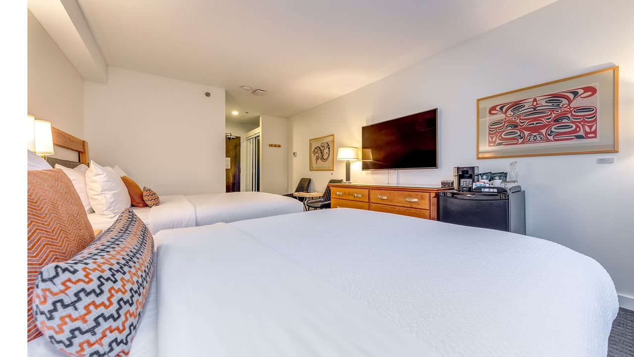 Two beds with pillows, a TV, and a framed Indigenous artwork on the wall in a hotel room.