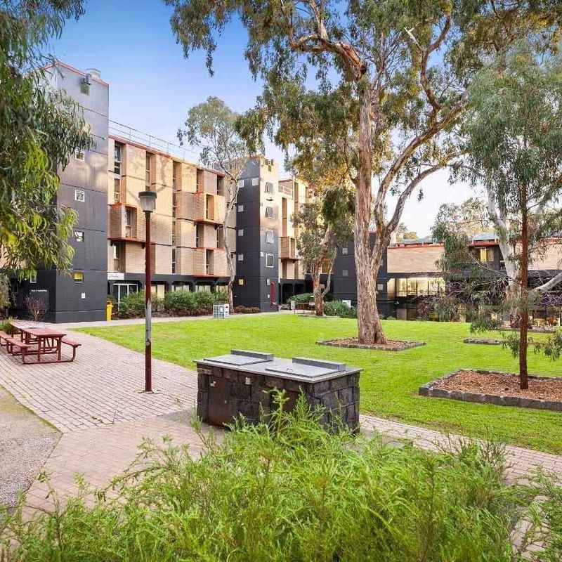 Exterior of La Trobe University – Menzies College with trees, grassy area, and picnic table.
