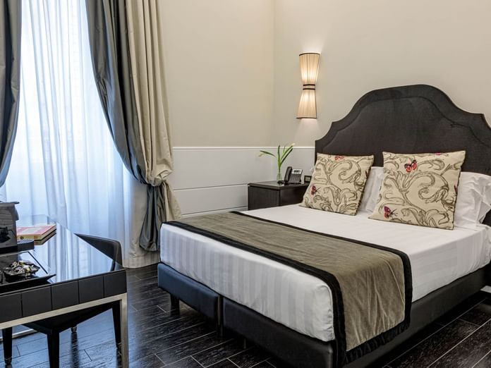 Stylish Smart Room at The Independent Suites with a double bed, modern lamp, desk, and soft natural light through curtains