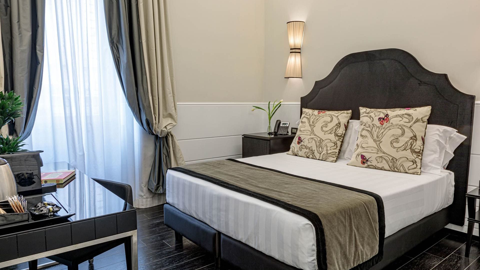 Stylish Smart Room at The Independent Suites with a double bed, modern lamp, desk, and soft natural light through curtains