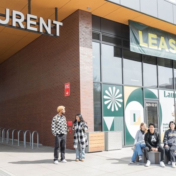 Students standing and sitting outside the entrance of Laurent student apartments.