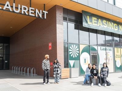 Students standing and sitting outside the entrance of Laurent student apartments.