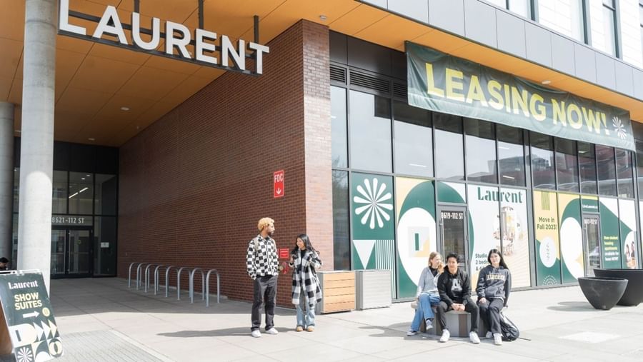 Students standing and sitting outside the entrance of Laurent student apartments.