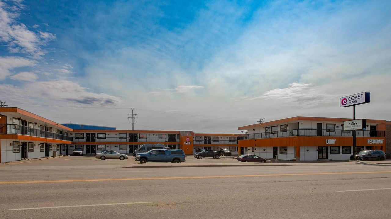 Exterior view of Coast Dawson Creek Hotel with guest room balconies, parking and the hotel sign.
