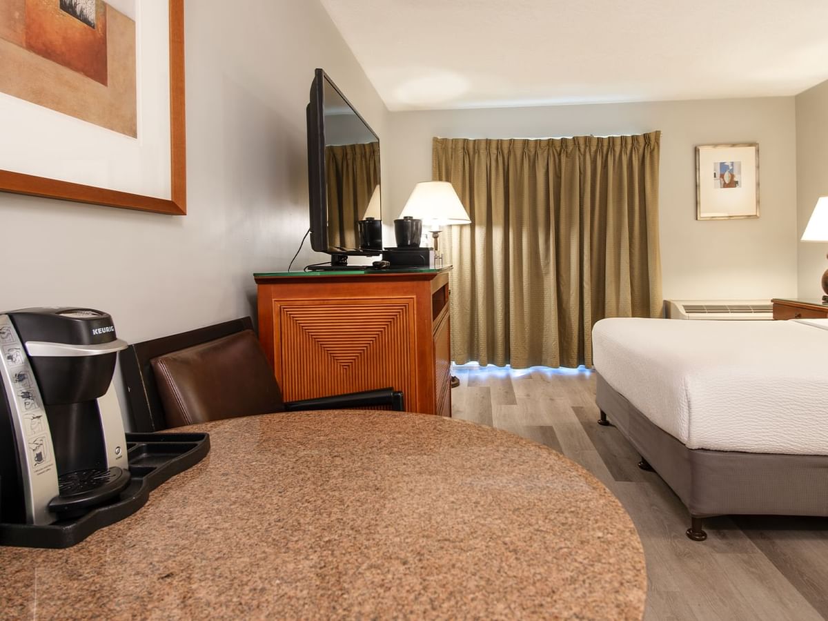 Hotel guestroom with queen bed, TV, table and coffee machine