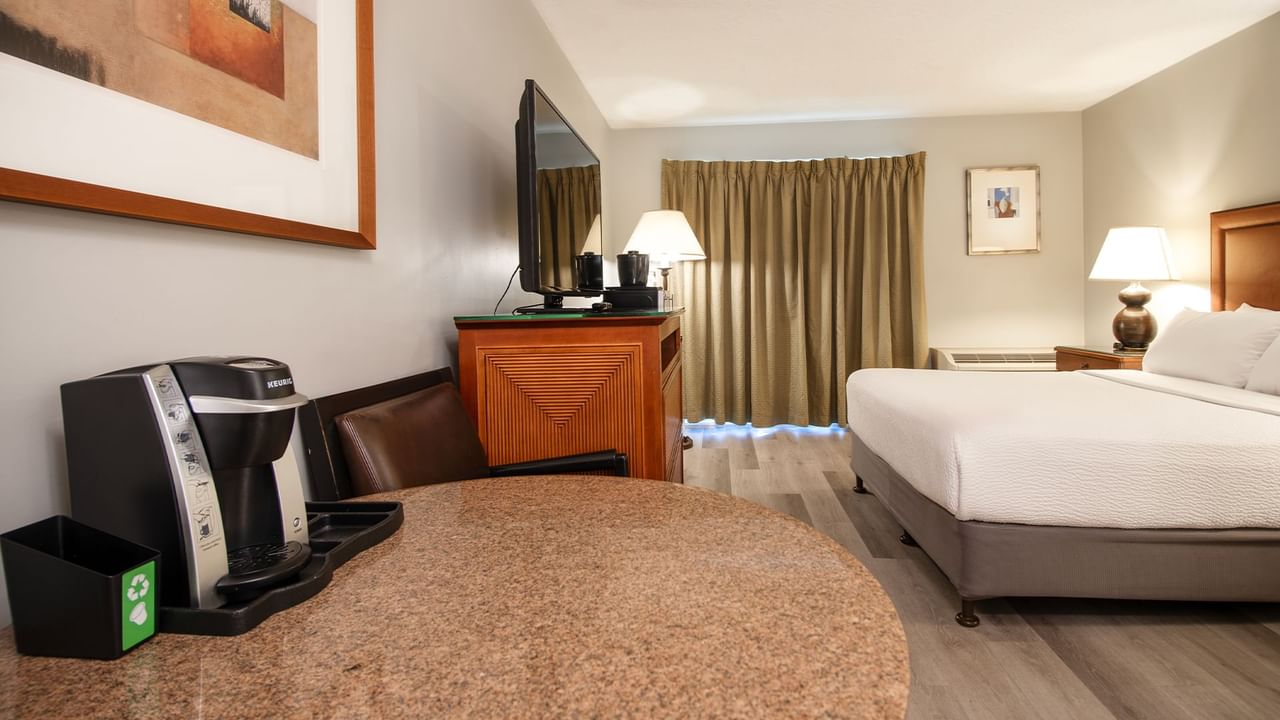 Hotel guestroom with queen bed, TV, table and coffee machine