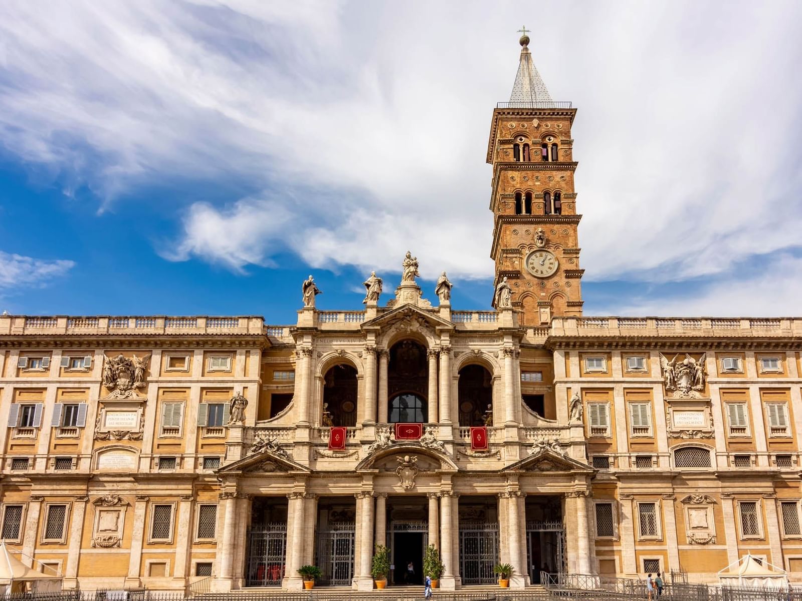 Ornate facade of Santa Maria Maggiore, with a tall clock tower, and a vibrant blue sky near The Guardian Hotel