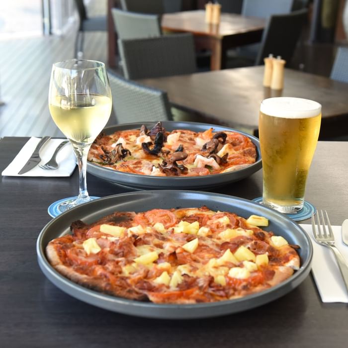 Two pizzas with a white wine and a beer served on a table in Celsius Restaurant & Bar at Mercure Hotel Townsville