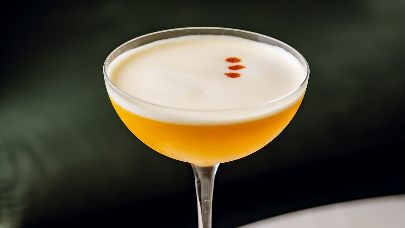 A cocktail glass with white foamy top and orange liquid on a white table at Warwick Hotels and Resorts 