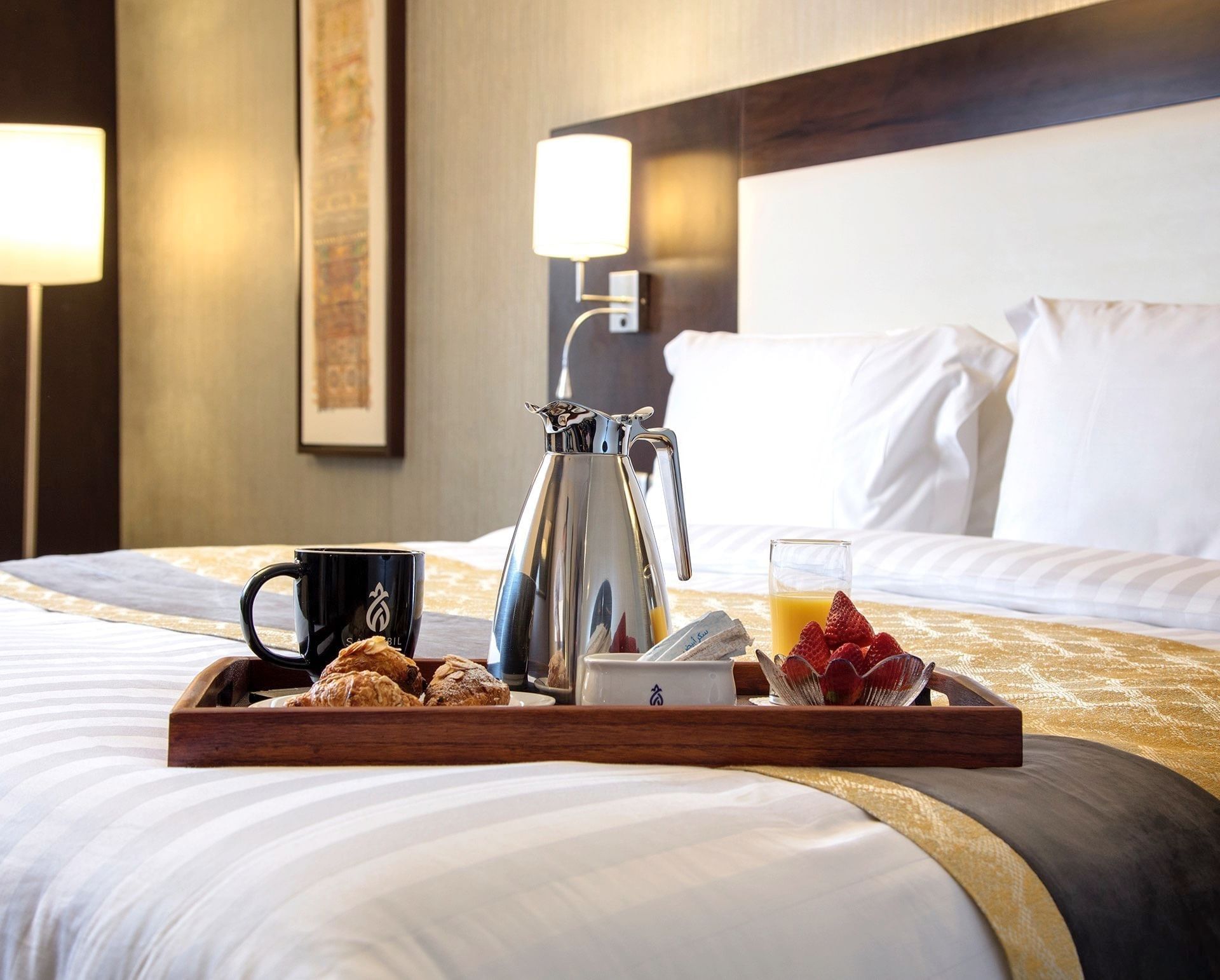 Breakfast tray on a bed with a silver coffee pot, orange juice, & croissants in the Deluxe Room at Warwick Hotel Jeddah