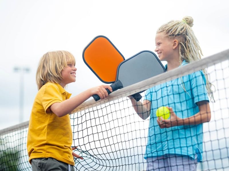 Dos niños felices jugando pickleball cerca de Fiesta Americana Funeeq bajo un día soleado con paletas coloridas