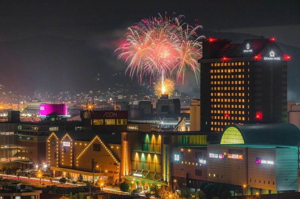 Colorful fireworks exploding in night sky above illuminated city buildings and Grand Park Otaru