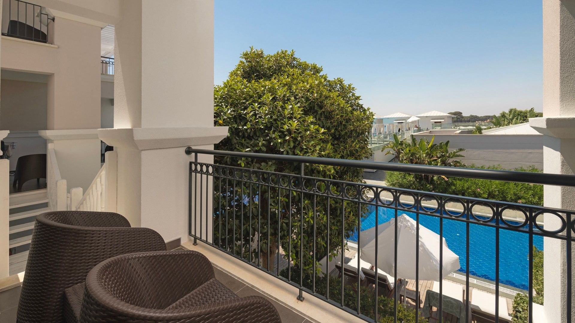 Balcony with wicker seating overlooking pool and lush gardens at Titanic Deluxe Golf Belek, Antalya.