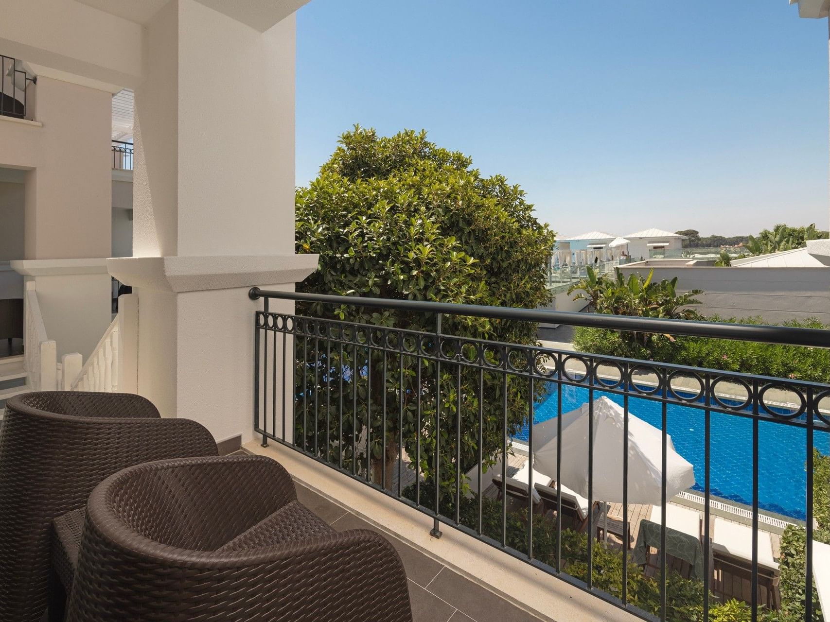 Private balcony with wicker seating overlooking a blue pool and lush greenery at Titanic Deluxe Golf Belek