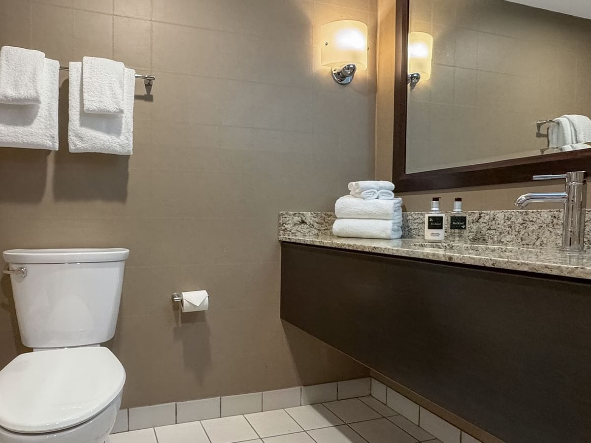 Modern bathroom with white toilet, large mirror, granite sink with faucet, and towels.