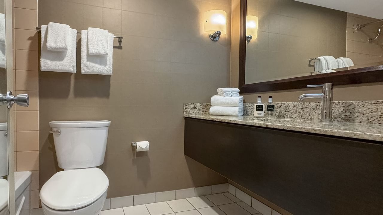 Modern bathroom with white toilet, large mirror, granite sink with faucet, and towels.