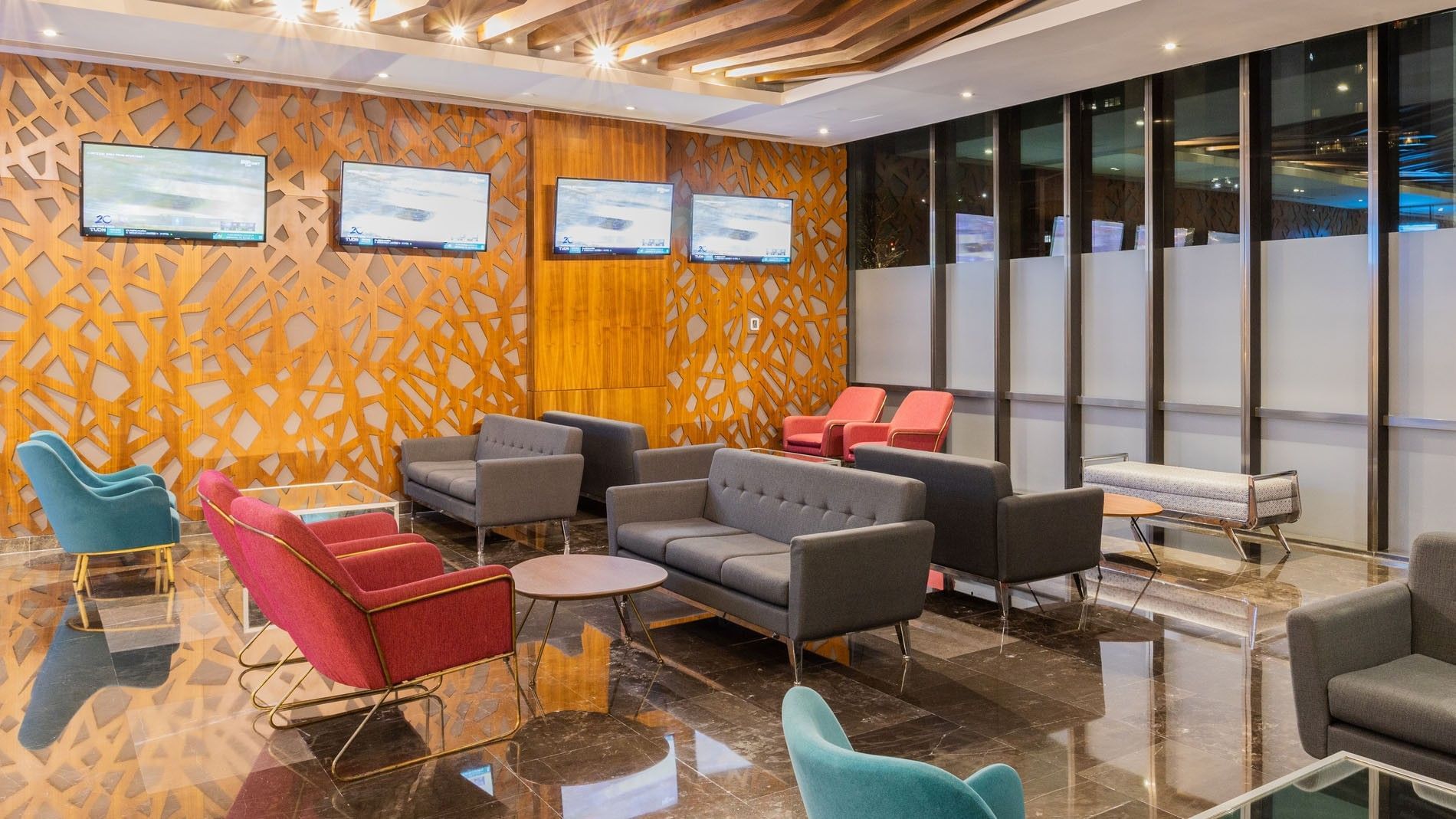 Hotel waiting lounge with wood lattice walls, gray sofas, and several TVs at Camino Real Fashion Drive, Monterrey
