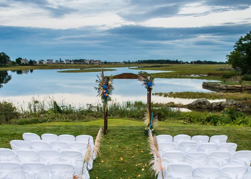 Outdoor wedding ceremony set up with white chairs facing a wooden arch at Ogunquit Collection