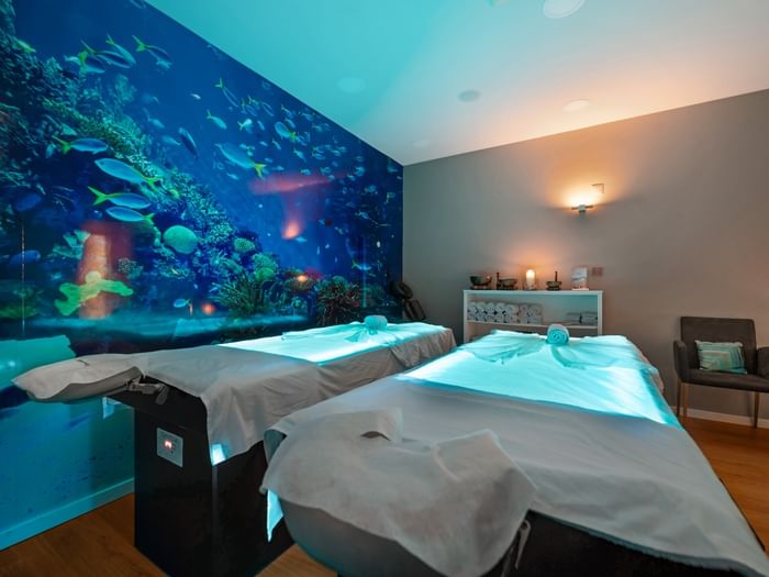 The tranquil couples spa room at Hotel Do Caracol, featuring glowing massage tables and an aquatic mural