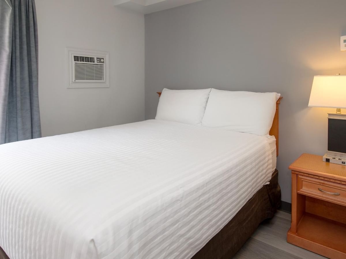 A bedroom with a bed, a nightstand with a lamp, and a window with curtains.